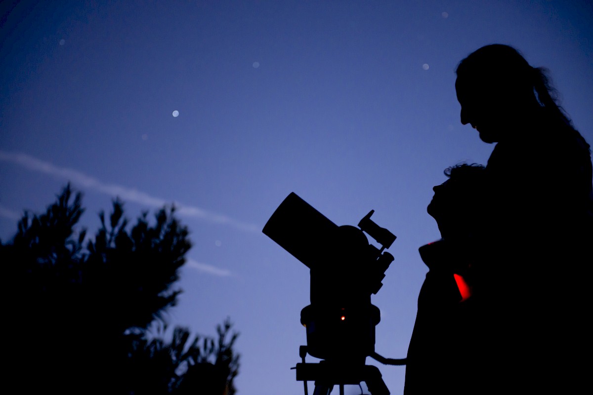 People are watching the night sky, using a telescope to observe the stars and planets.