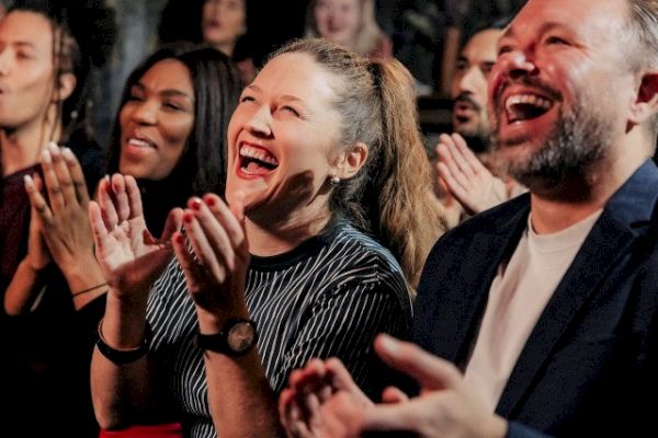 A group of people are clapping and laughing, suggesting they are enjoying a live performance or an event, creating a joyful atmosphere.