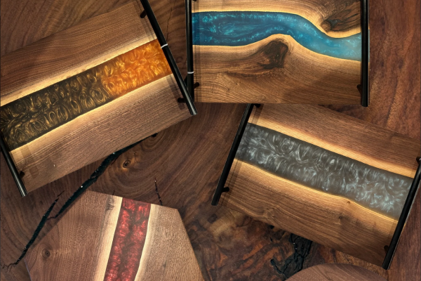Artisan resin and wood charcuterie boards with vibrant resin inlays in shades of blue, orange, red, and gray are arranged on a wooden surface.