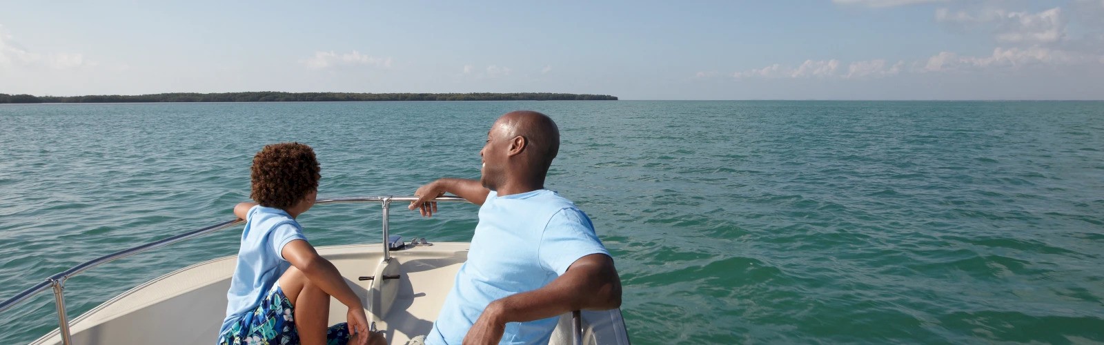 Two people are sitting on a boat, enjoying the expansive view of the calm sea under a clear sky.