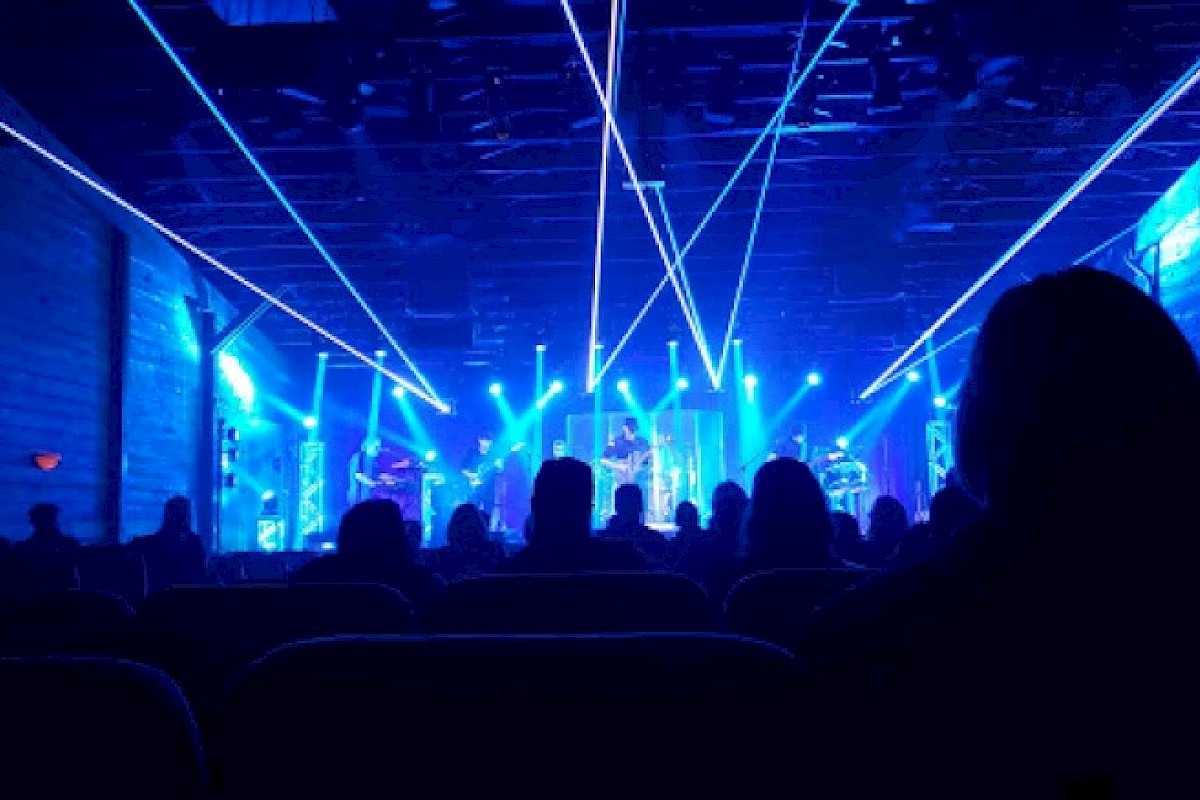 A live music concert with vibrant blue laser lights and silhouettes of the audience enjoying the show.