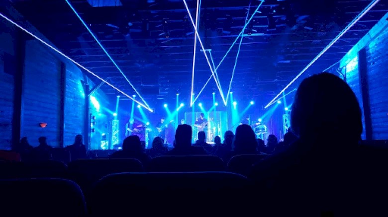 A live music concert with vibrant blue laser lights and silhouettes of the audience enjoying the show.