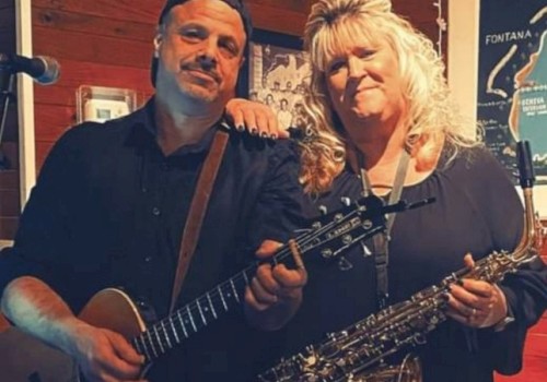 A man with a guitar and a woman with a saxophone pose together indoors, marked 