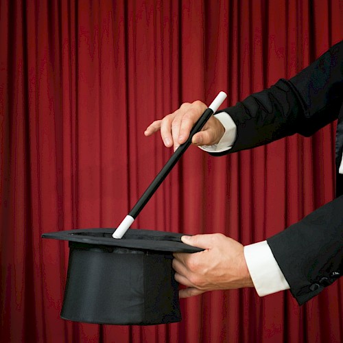 A magician is holding a top hat and a wand against a red curtain backdrop, suggesting a magic trick about to be performed.